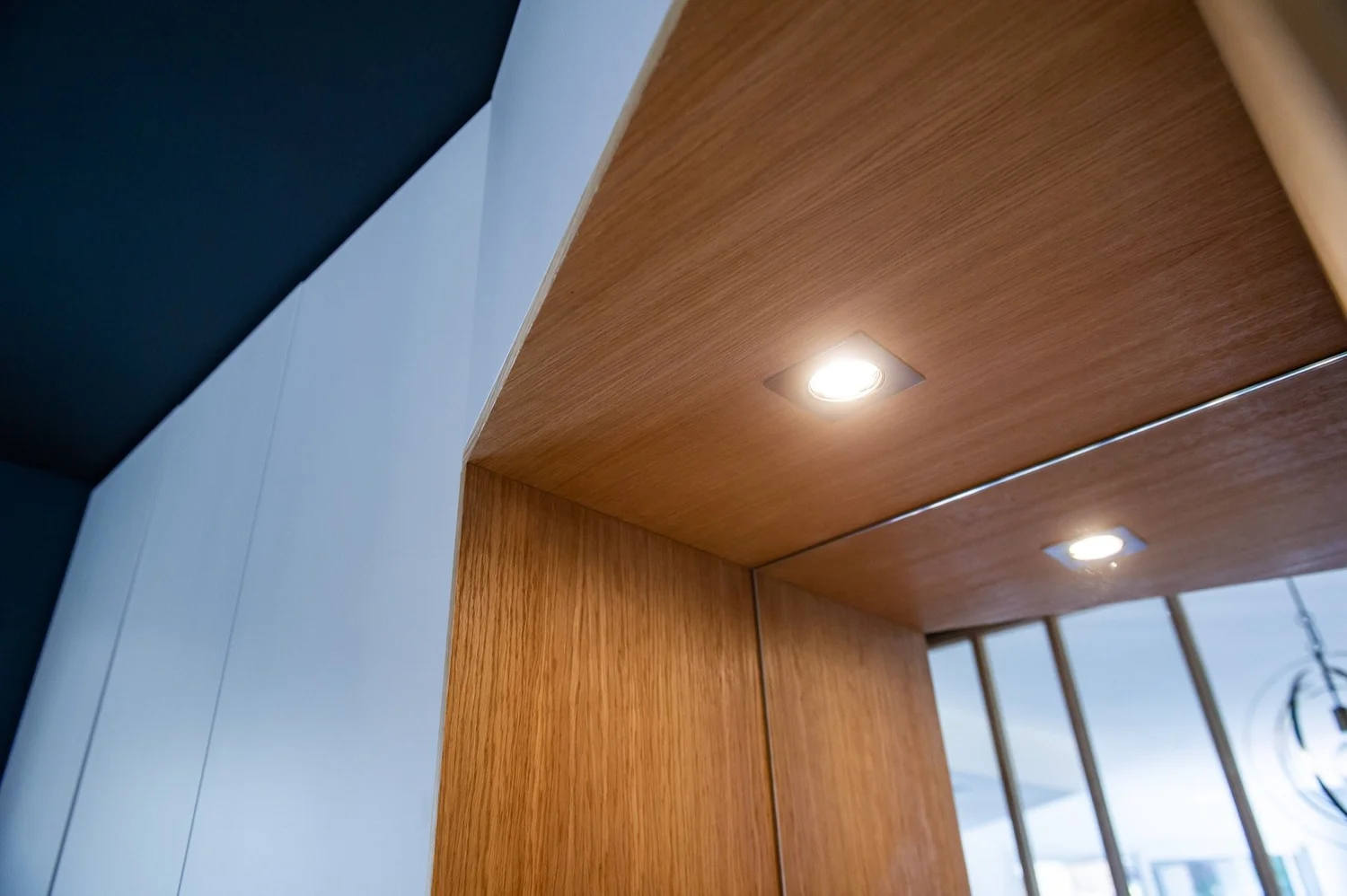Plafond en bois avec deux spots lumineux encastrés, près d'une fenêtre avec vue extérieure.