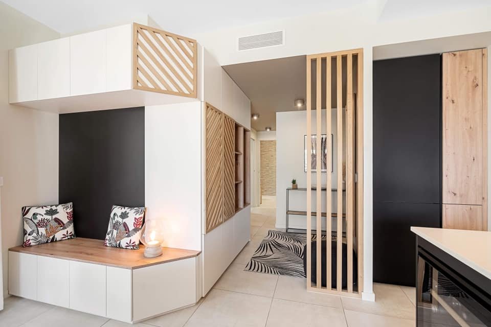Intérieur moderne avec coin lecture, banquette avec coussins à motifs floraux, séparation en bois et noircissement de mur pour délimiter les espaces.