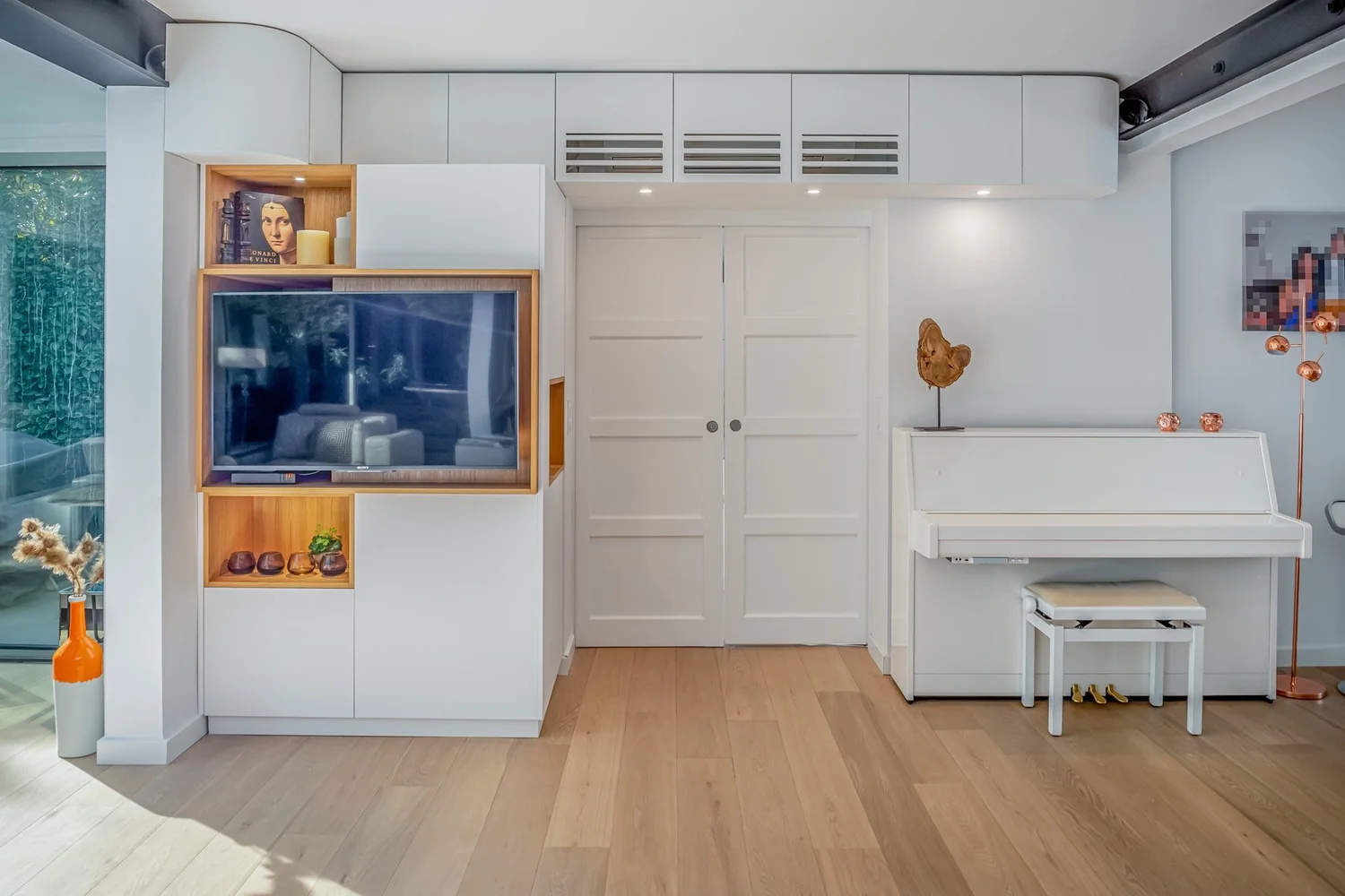 Intérieur moderne avec télévision, piano blanc, décor en bois, vase orange, œuvres d'art.