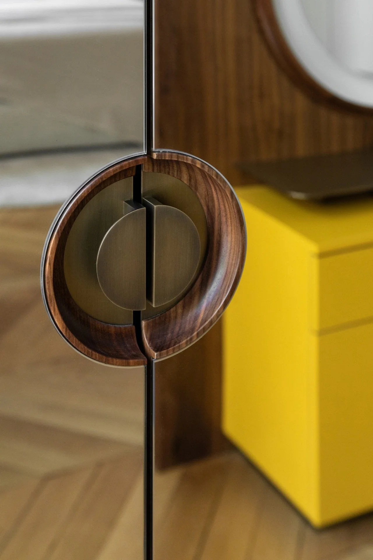 Une poignée de porte en métal doré, entourée de bois foncé, fixée sur une porte en miroir.