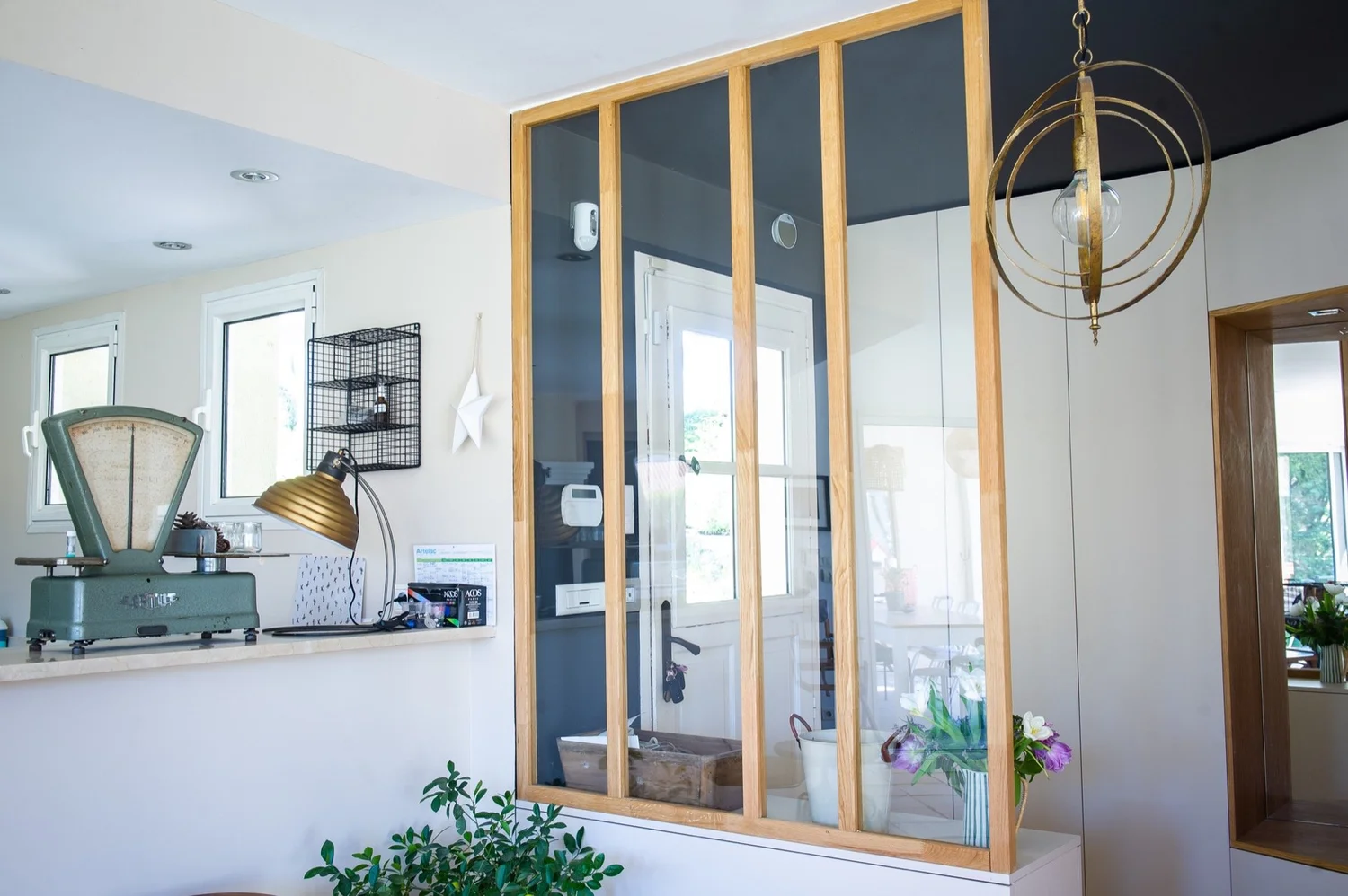 Intérieur moderne avec un comptoir de cuisine, un lampadaire, une étagère en métal, une décoration en forme d'étoile, une fenêtre, un espace de travail avec un vélo d'intérieur, une cloison en verre avec une structure en bois, des plantes et une lamp