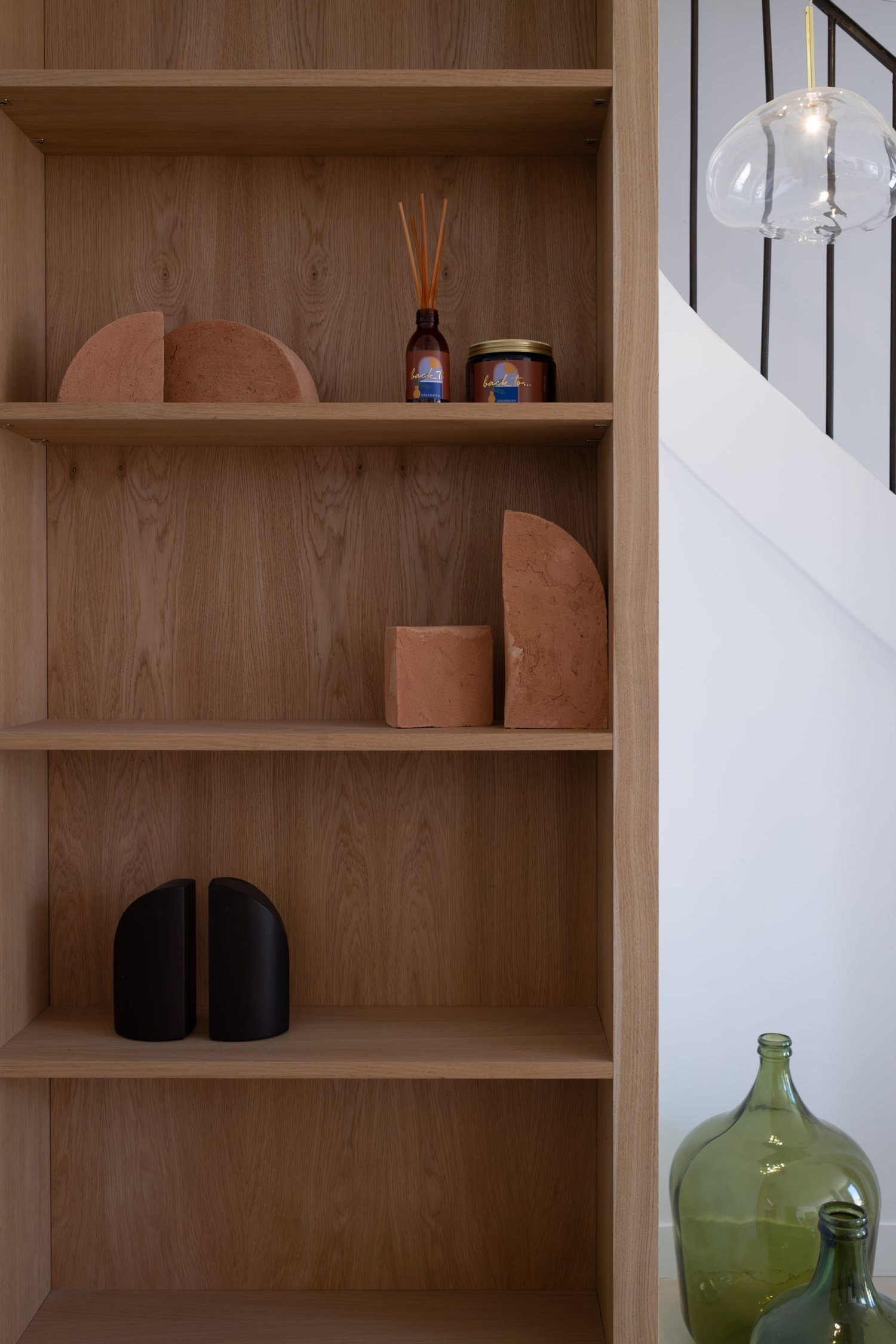 Une étagère en bois avec des objets décoratifs en argile, verre, et divers petits contenants, en intérieur.