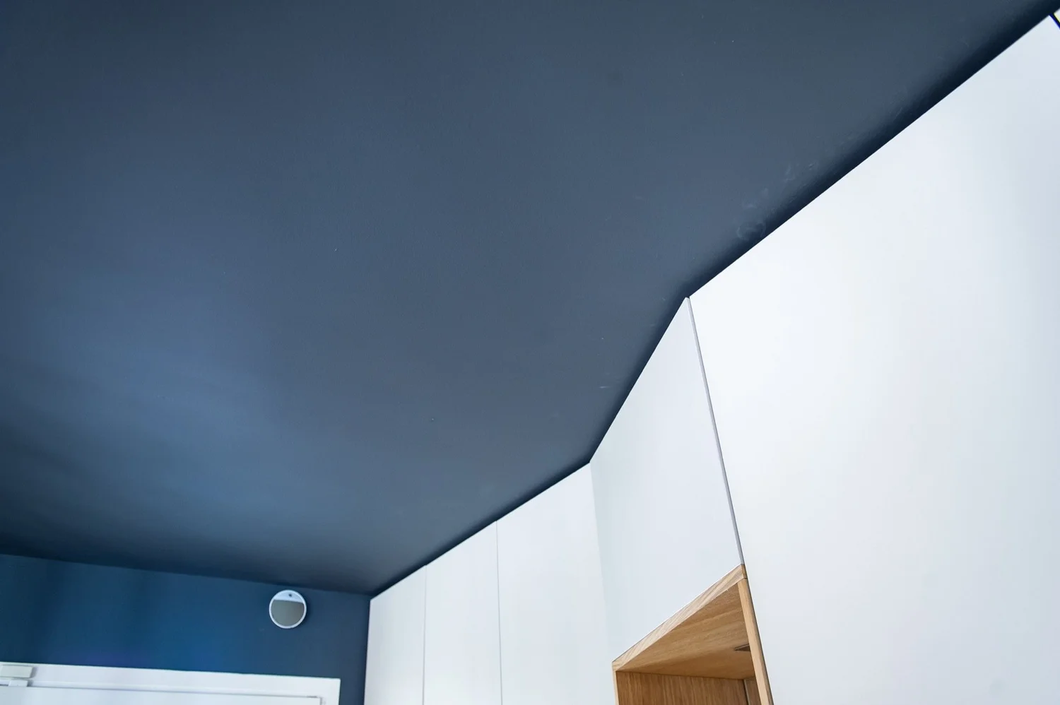 Plafond et murs d'une pièce moderne avec un mur bleu foncé, un mur blanc et une hotte de cheminée en bois.