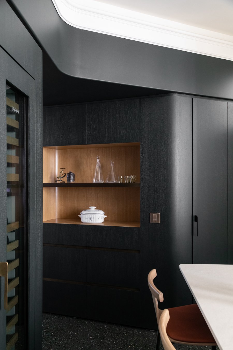 Un coin de cuisine moderne avec un mur noir, une étagère en bois contenant des verres, une casserole blanche en céramique, et un meuble intégré noir.