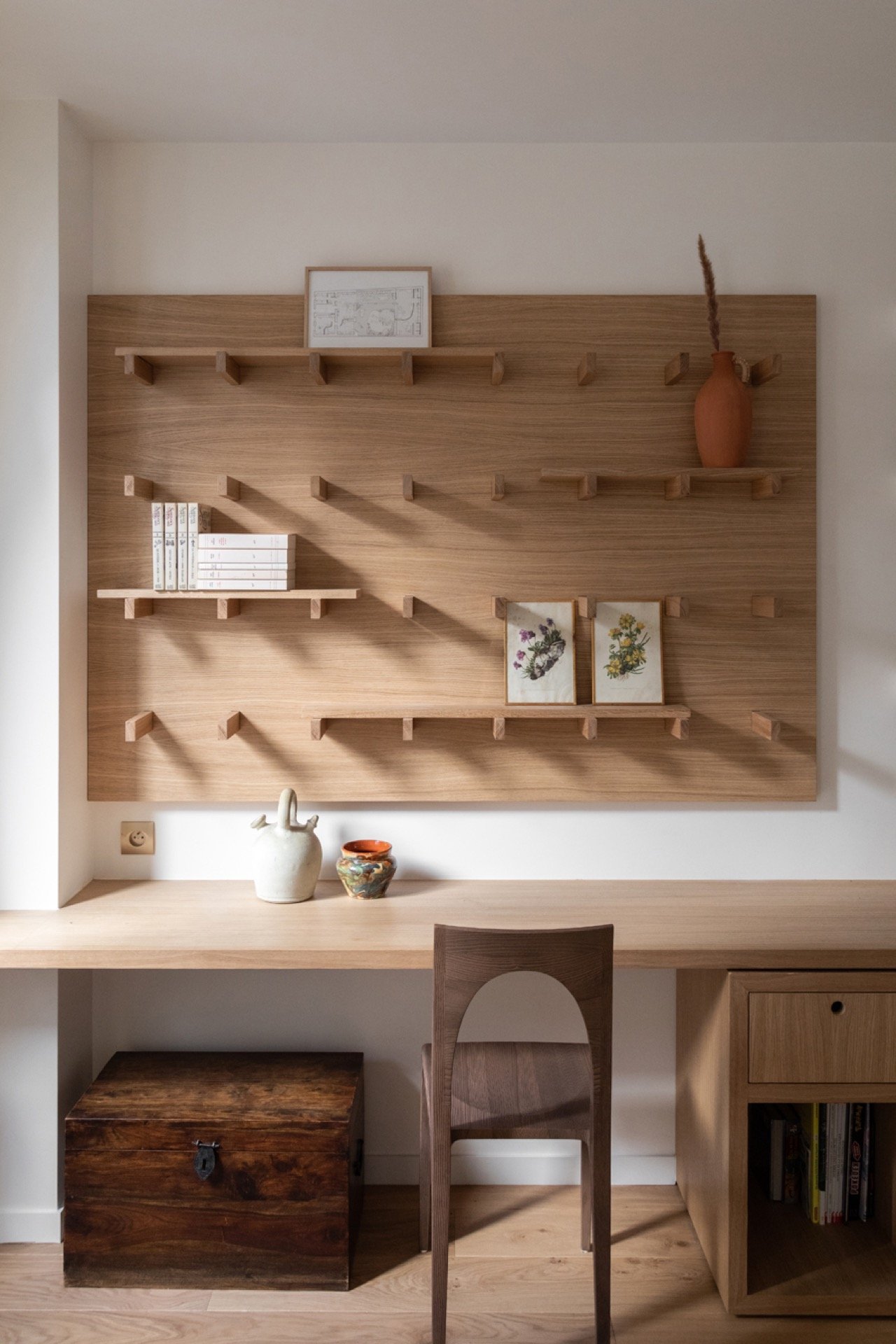 Mur en bois avec étagères, décorations en céramique, livres, plans, vases et une commode en bois dans un espace de bureau ou de lecture.