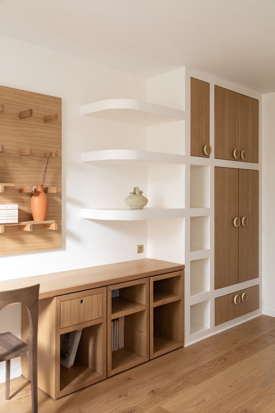Intérieur d'une pièce moderne avec mobilier en bois clair, étagères blanches et murs blans.