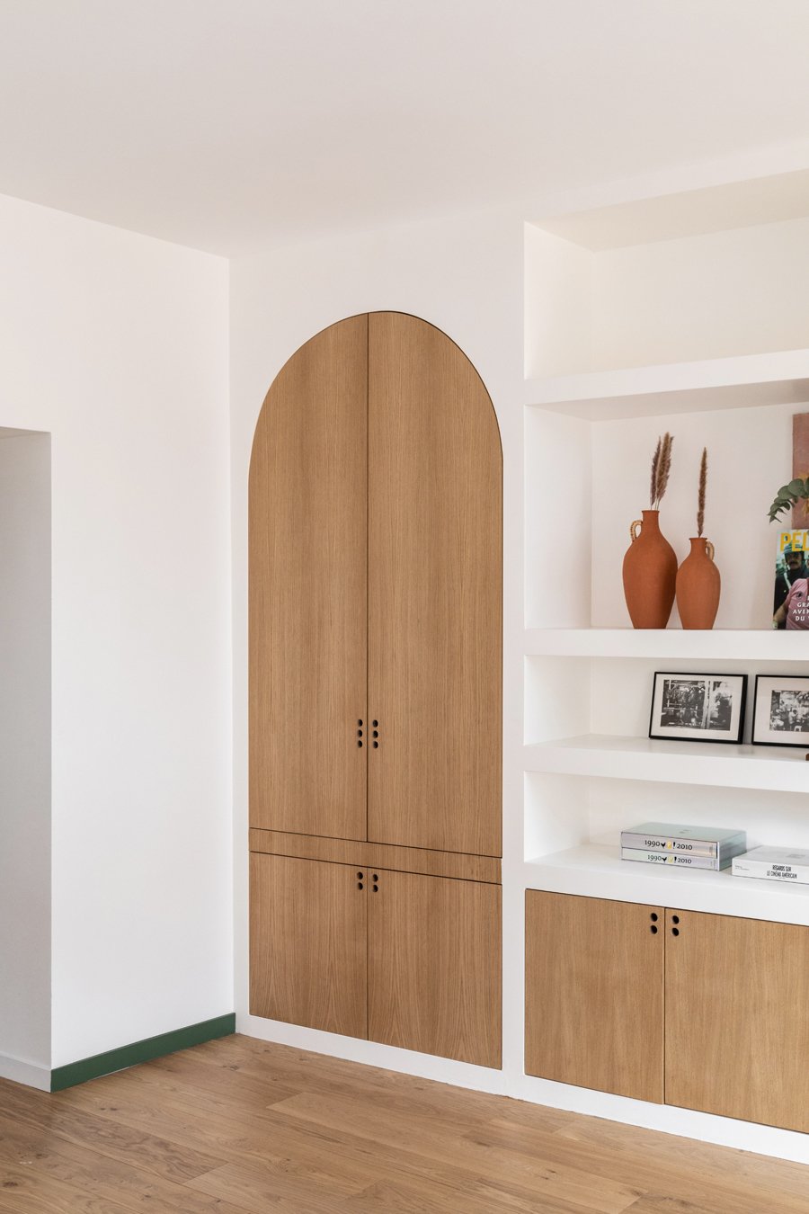 Intérieur d'une pièce moderne avec un meuble en bois clair intégré dans un mur blanc, décoré avec deux vases en terre cuite et des cadres photo en noir et blanc.