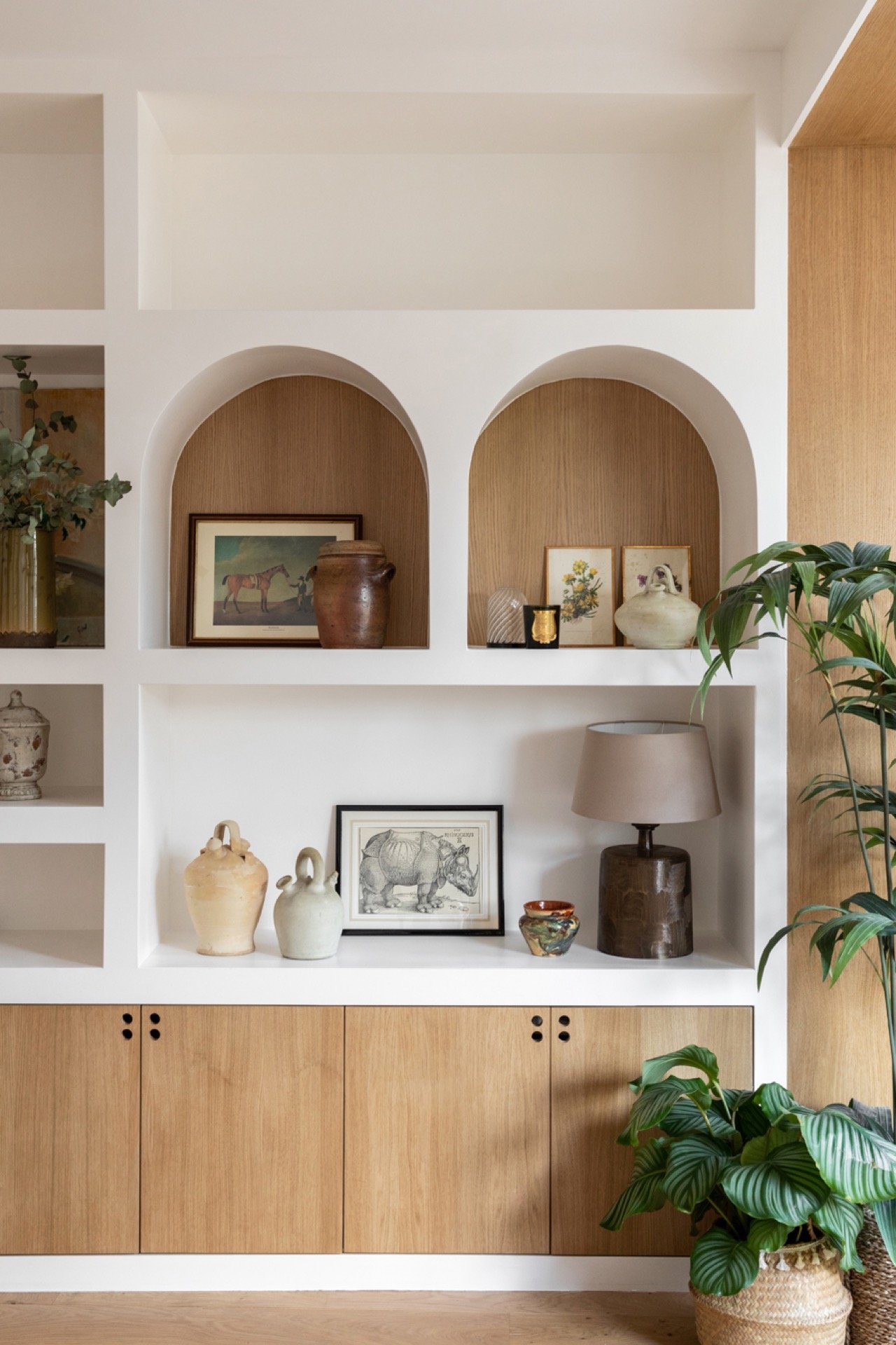 Etagère décorative avec des vases, tableaux, et une lampe, avec une plante verte à droite.