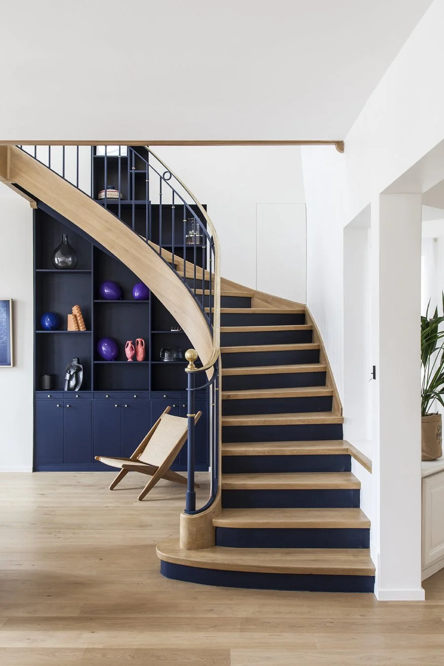 Escalier en bois avec rampe noire dans intérieur moderne avec bibliothèque bleue et décoration