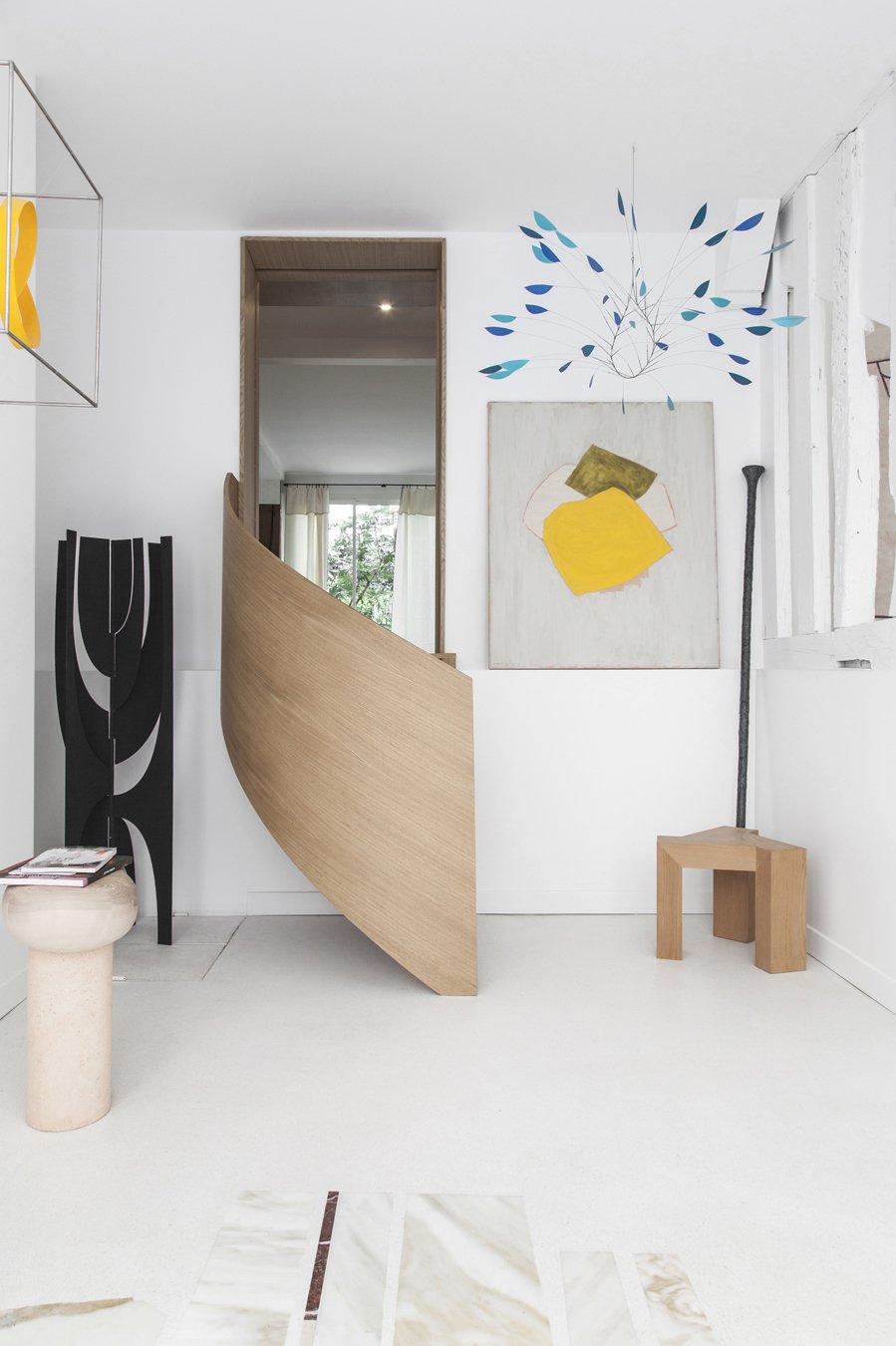 Intérieur minimaliste avec des œuvres d'art modernes, un mur blanc, un panneau en bois incurvé, et un petit banc en bois.