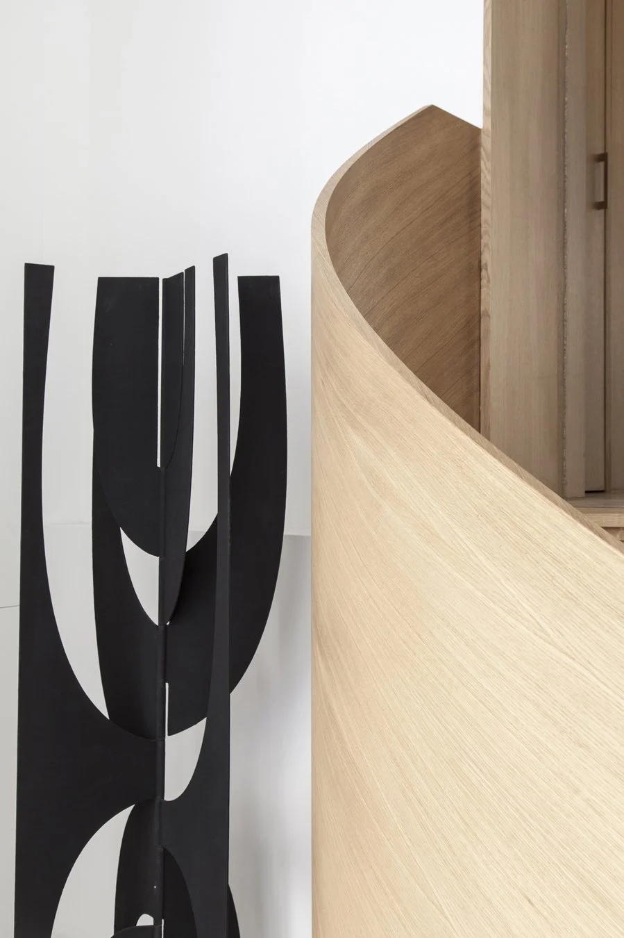 Une sculpture noire abstraite en métal et un meuble en bois clair avec une surface courbée.