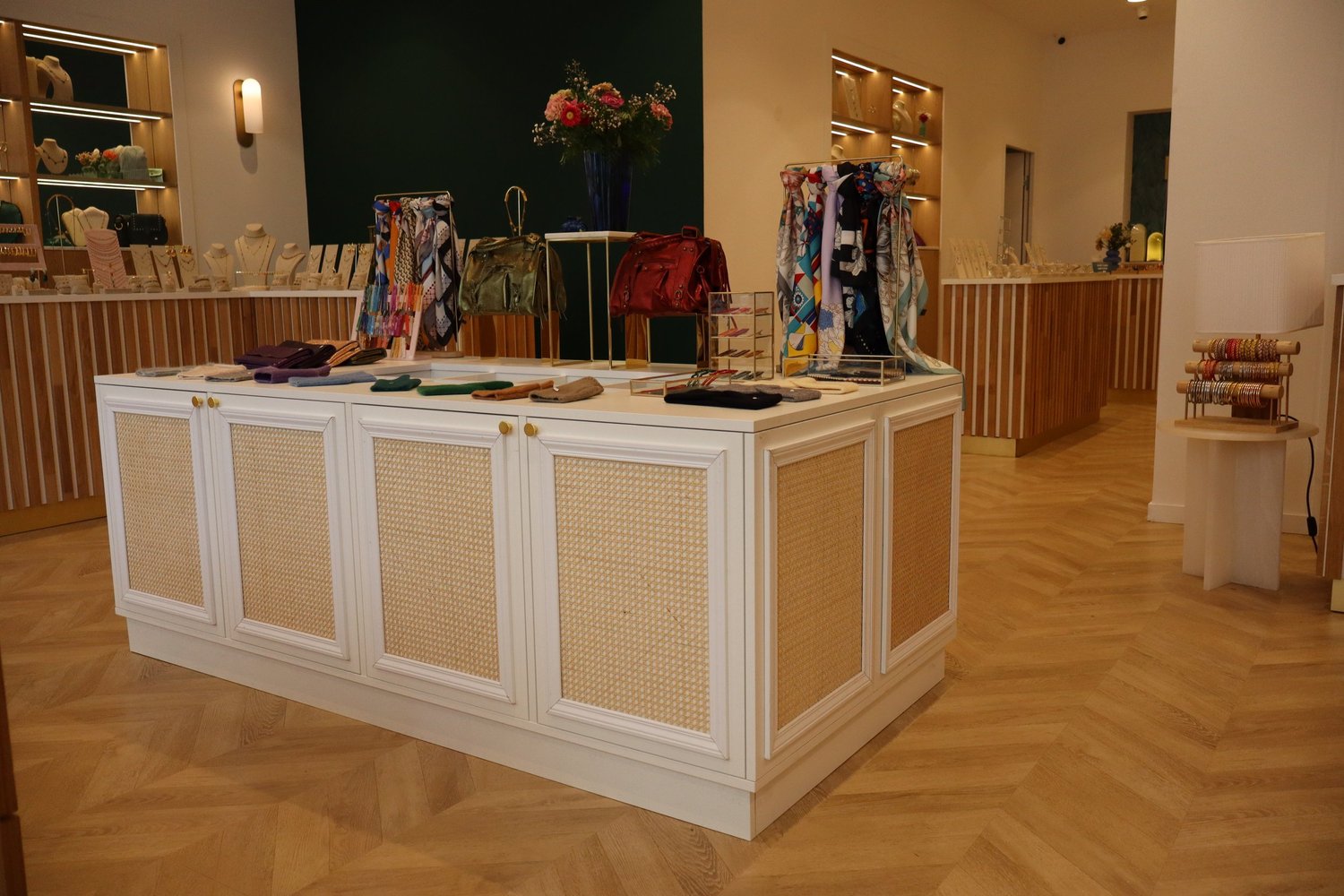 Vitrine de boutique de mode avec sacs, foulards et bijoux. Décoration florale dans le fond, sol en parquet.