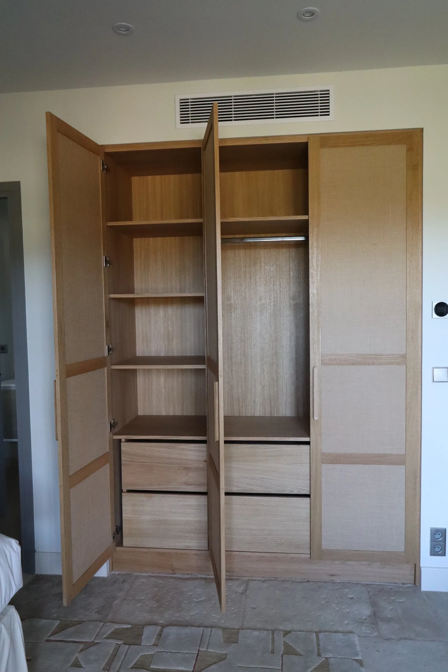 Grand placard en bois avec portes ouvertes, montrant des étagères, un rail pour vêtements et des tiroirs en bas.