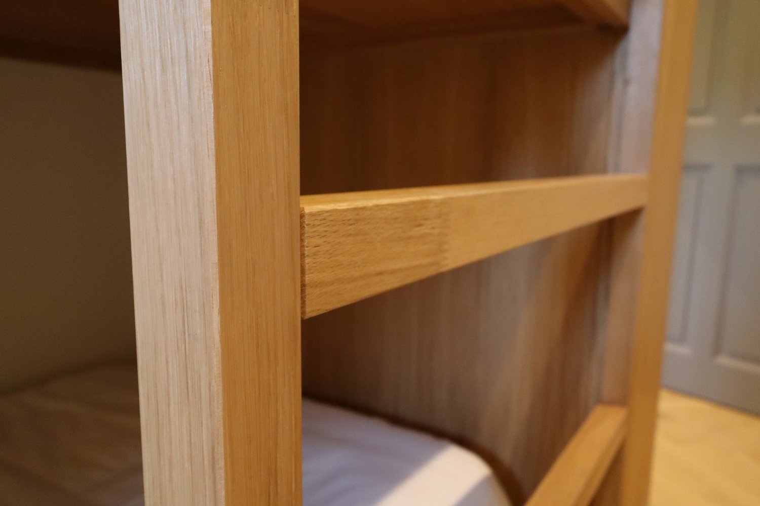 Vue en gros plan d'une étagère en bois clair dans une bibliothèque ou une armoire, avec une porte en arrière-plan.