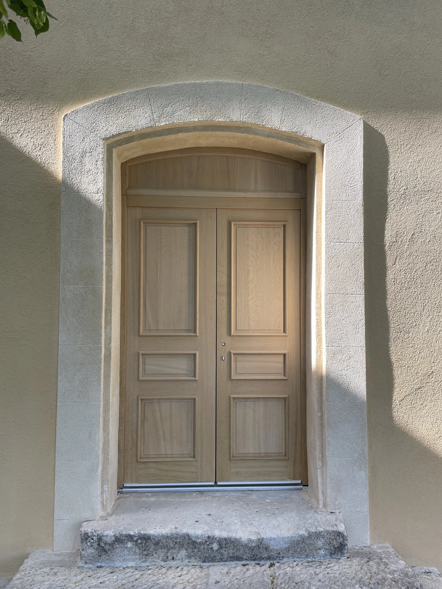 Porte en bois double avec une arche en pierre au-dessus, dans un mur beige.