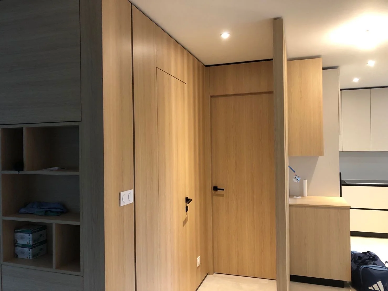 Intérieur d'une pièce moderne avec meubles en bois clair, portes en bois, et un espace de rangement ouvert avec quelques objets.