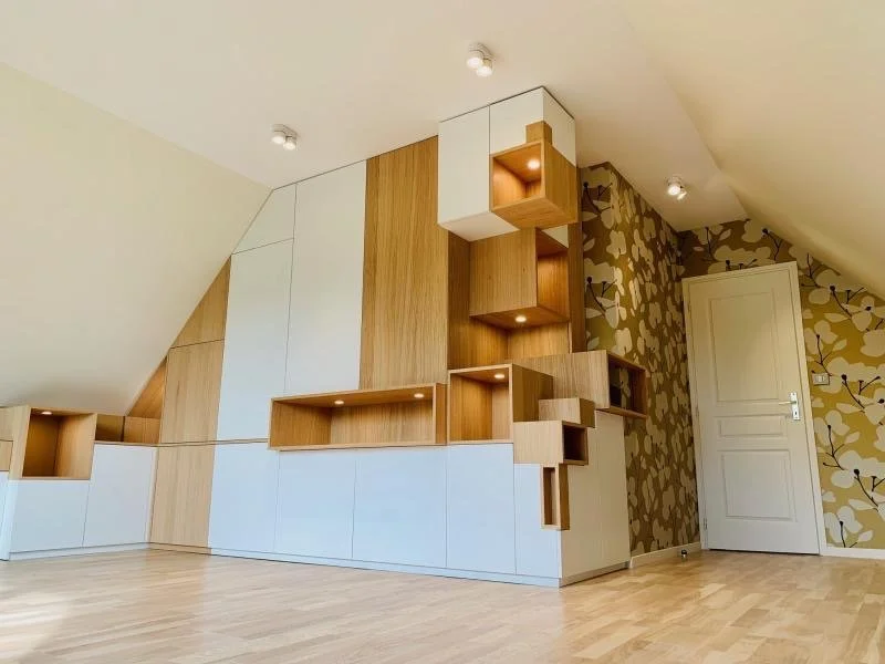 Mur avec étagères en bois et rangement blanc dans une pièce avec mur à papier peint floral et plafond en pente.