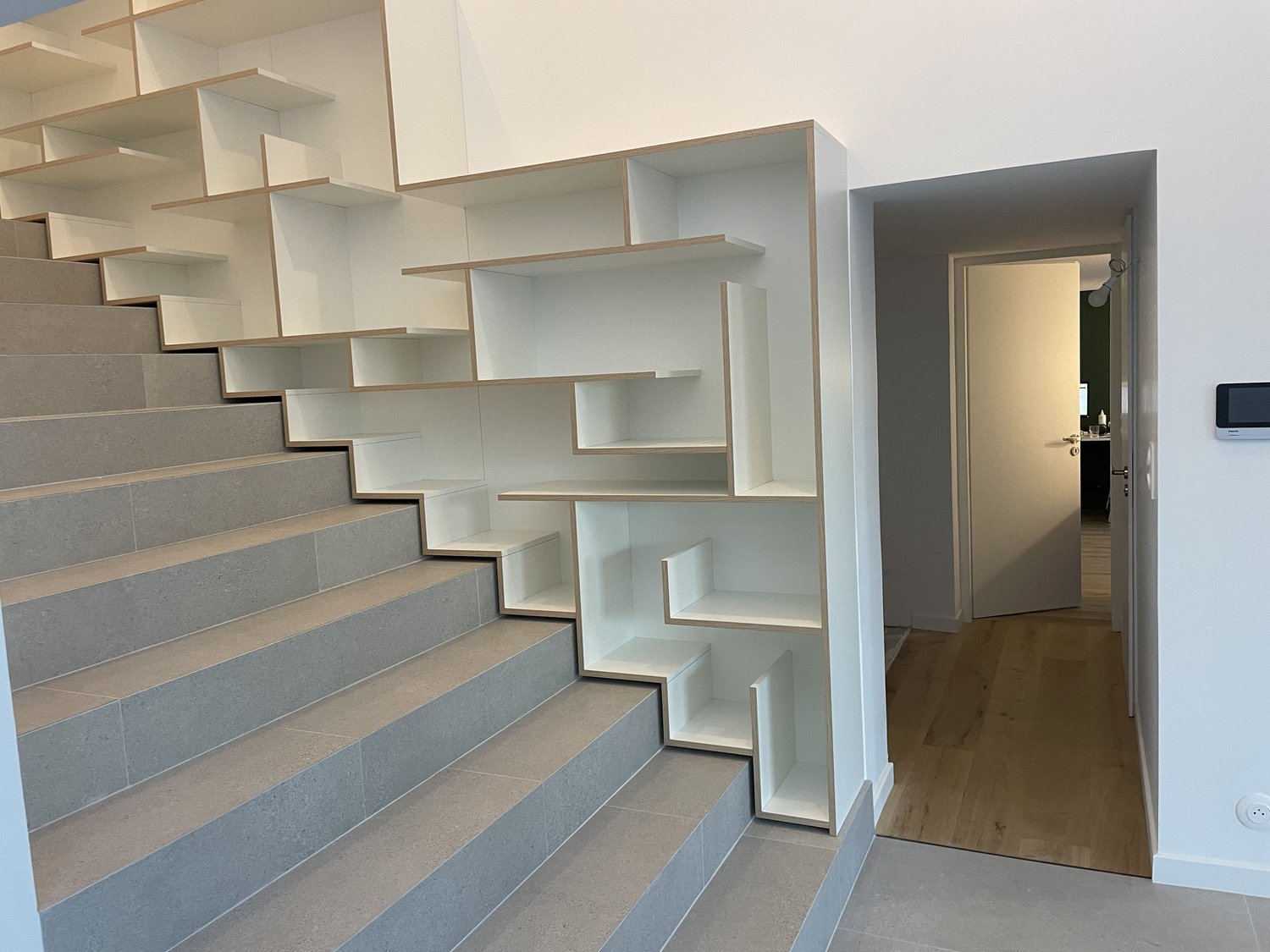 Escalier avec étagères intégrées en blanc, menant à un espace intérieur moderne et minimaliste.