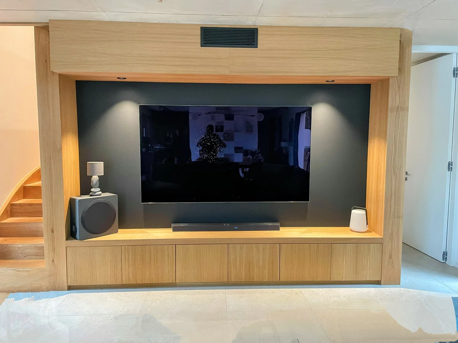 Écran de télévision encastré dans un mur en bois avec haut-parleur, lampe de chevet, et objets décoratifs.