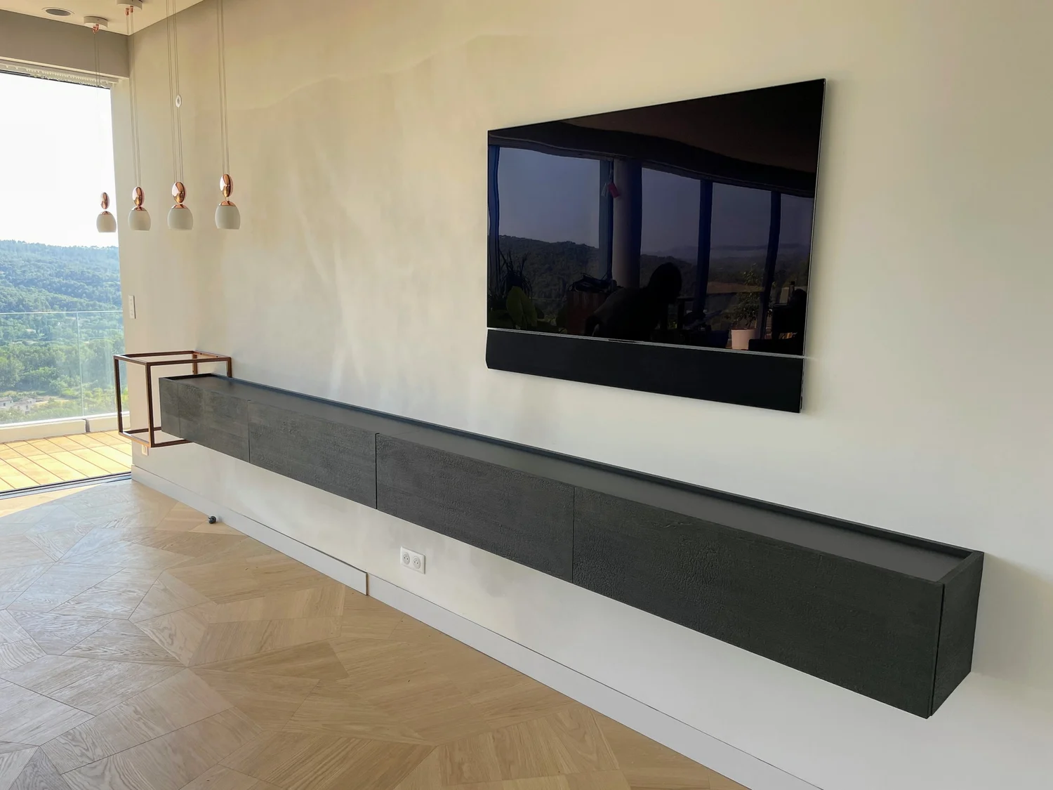 Salon moderne avec une télévision à écran plat noir, un meuble de rangement noir long et une pièce avec vue sur la nature.