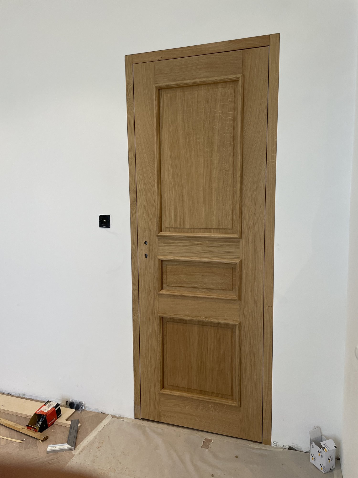 Une porte en bois installée dans un mur blanc, avec des outils de construction autour.