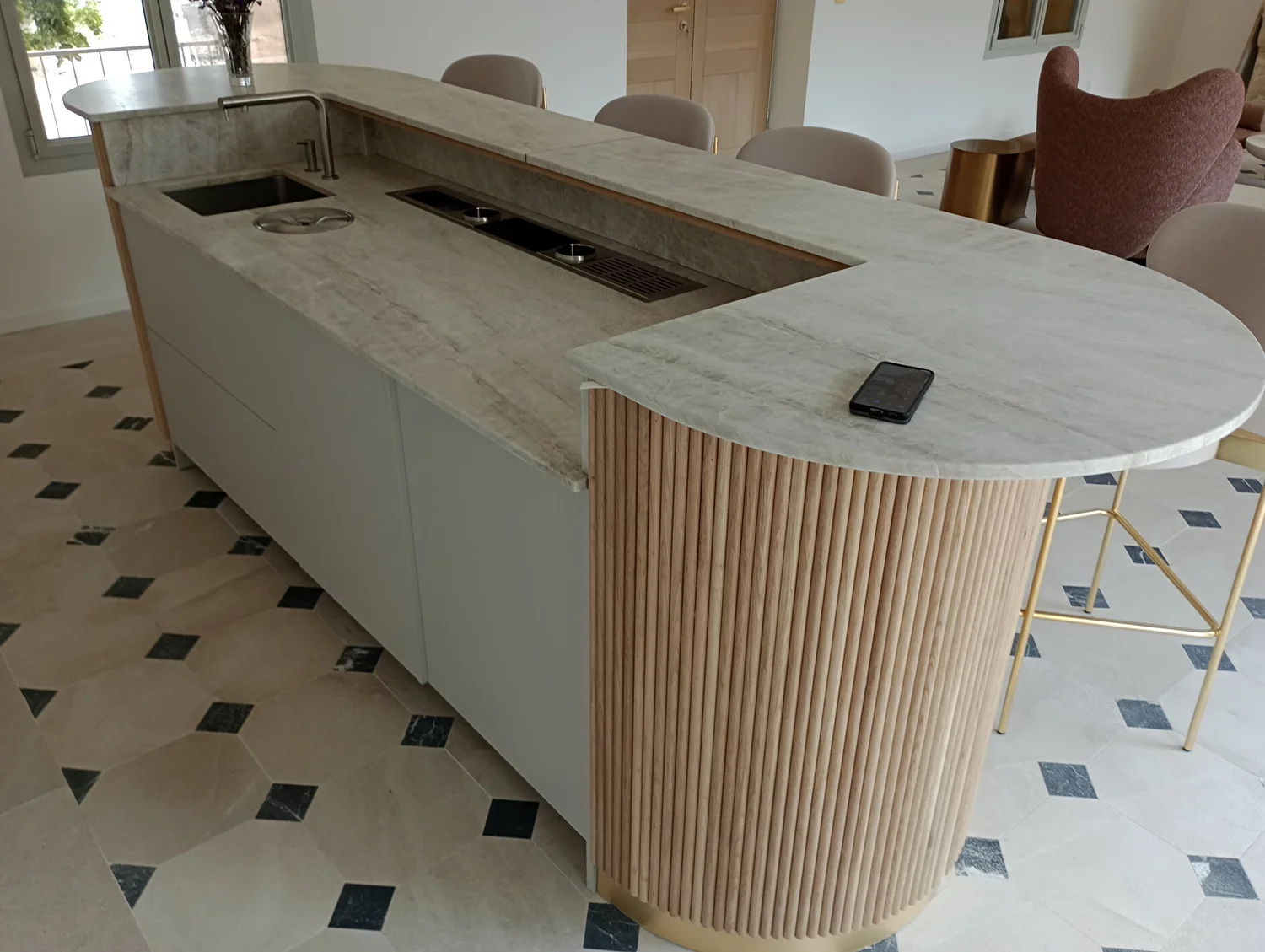 Îlot de cuisine moderne avec plan de travail en pierre, évier, plaque de cuisson intégrée, et un smartphone sur la surface