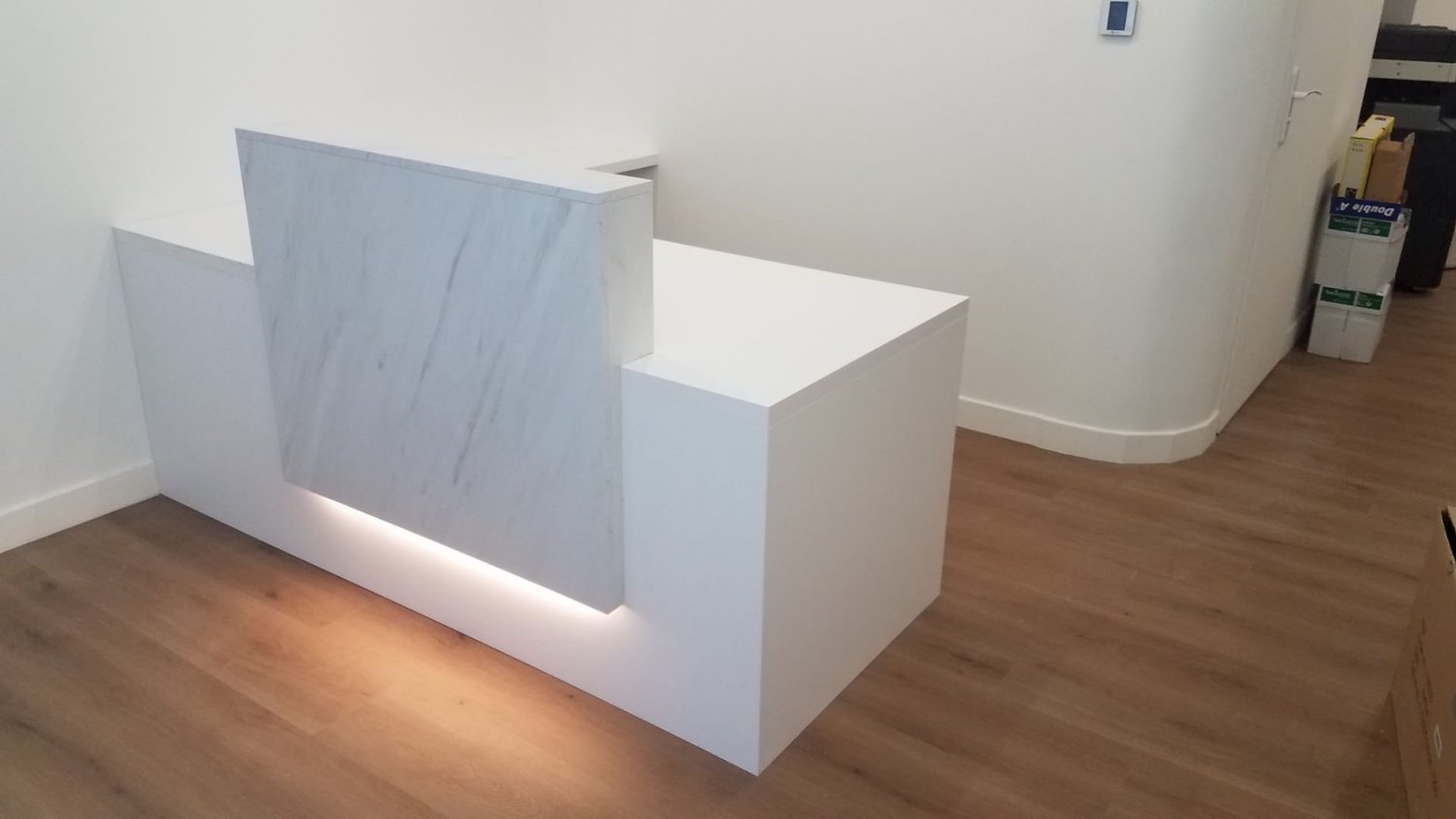 Une réception ou un comptoir en marbre blanc avec des lumières intégrées à la base dans un bureau ou un espace professionnel.
