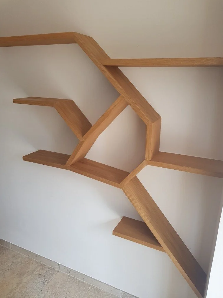 Une étagère en bois avec une conception géométrique sur un mur blanc, composée de plusieurs sections de différentes tailles et formes.»