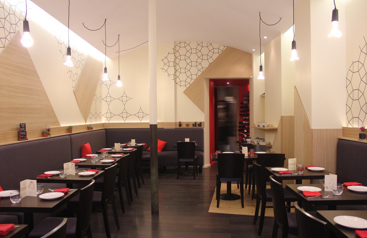 Salle à manger de restaurant avec des tables dressées, des chaises noires, un mur en bois clair, des suspensions lumineuses et des murs décorés avec des motifs géométriques