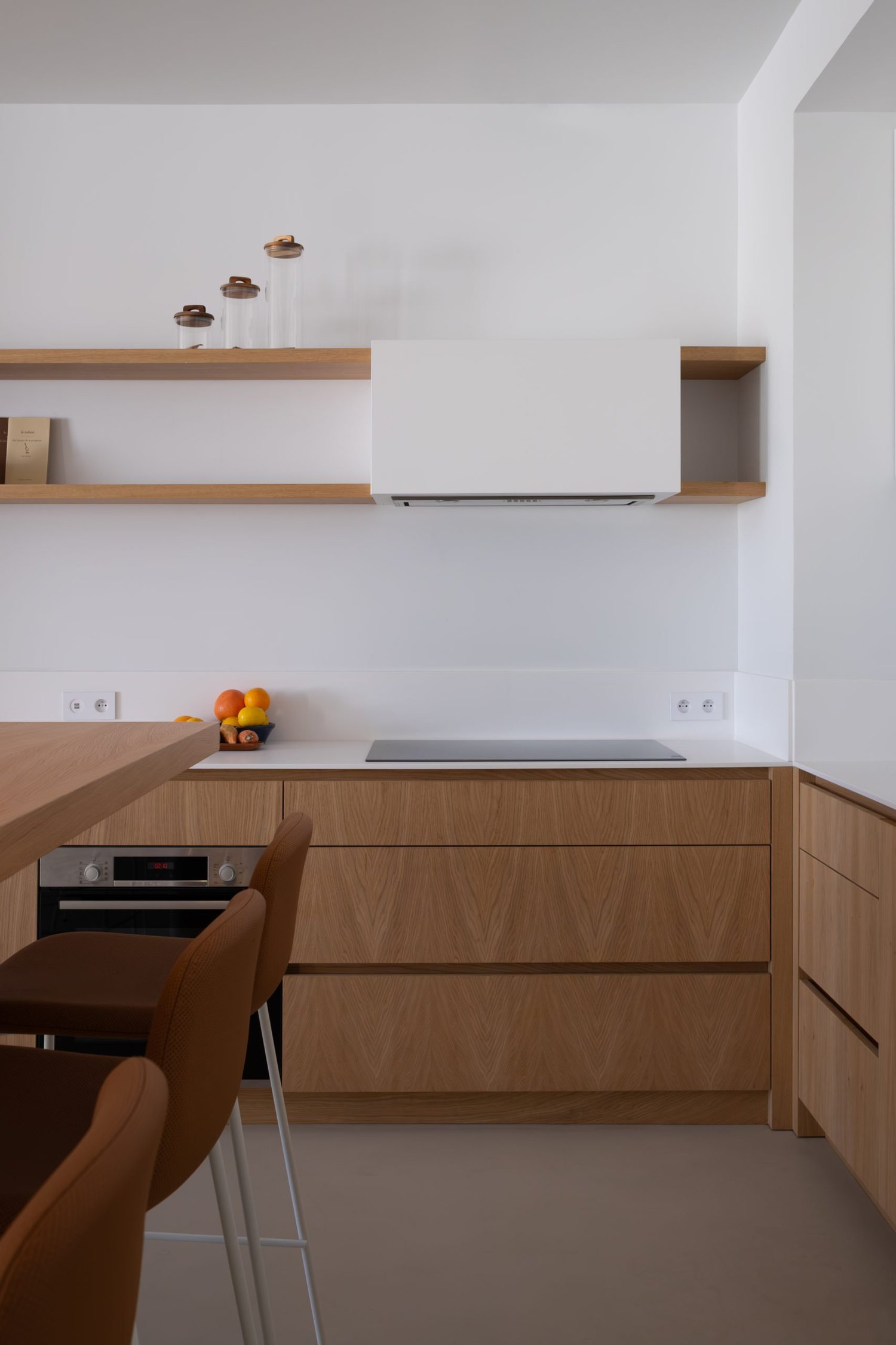 Cuisine moderne avec plan de travail en bois, étagères en bois, plaques de cuisson, four, et des fruits sur le comptoir