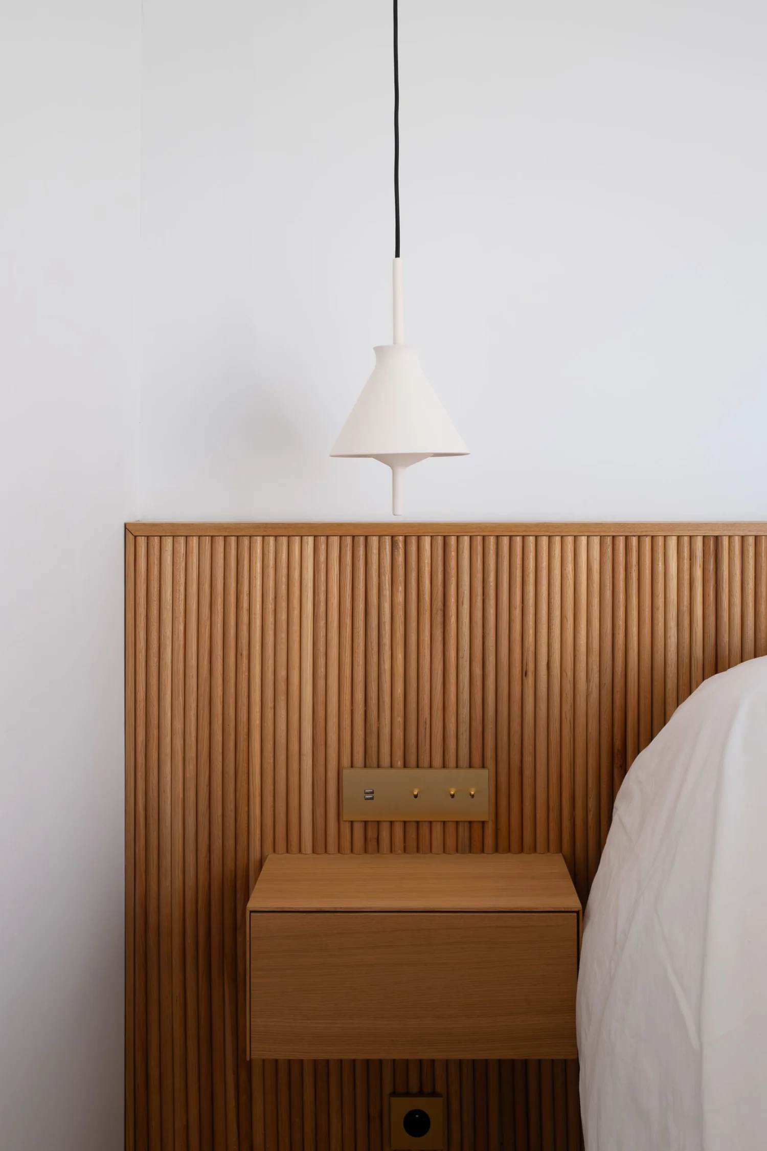 Lampe suspendue blanche au-dessus d'une tête de lit en bois avec un panneau de prises électriques intégré
